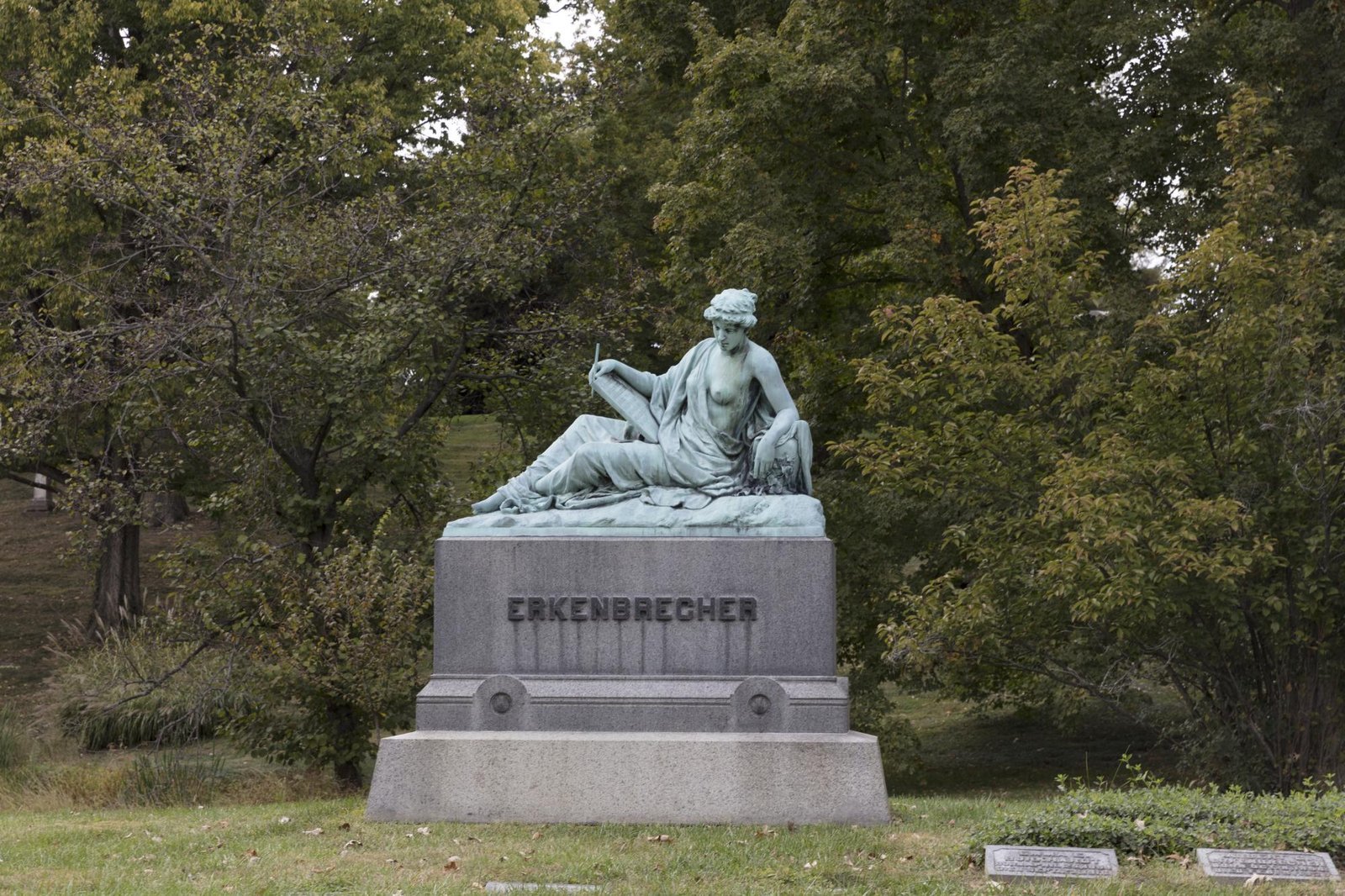 Reclining woman in green bronze with pen and tablet on a grey granite base among trees, Spring Grove Cemetery, Cincinnati