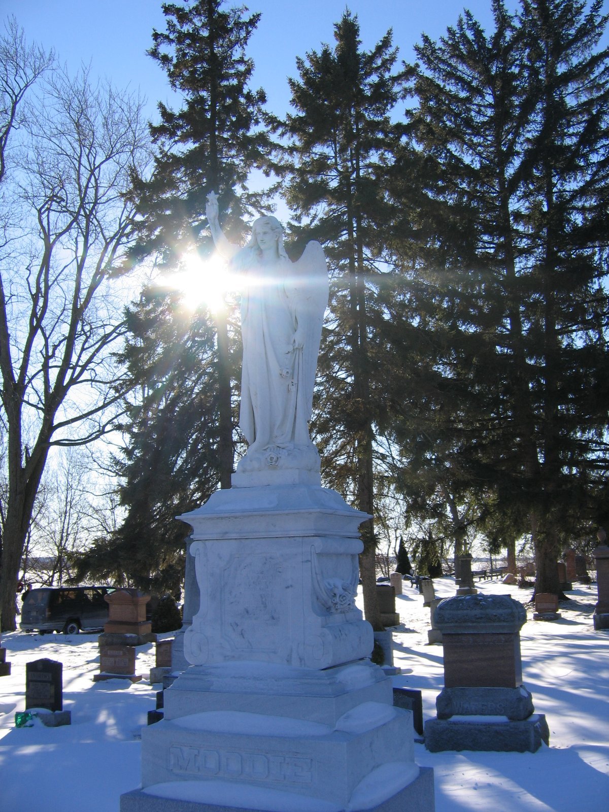 White stone angel statue with one arm raised on a tall carved pedestal in winter at Belleville Cemetery, Ontario