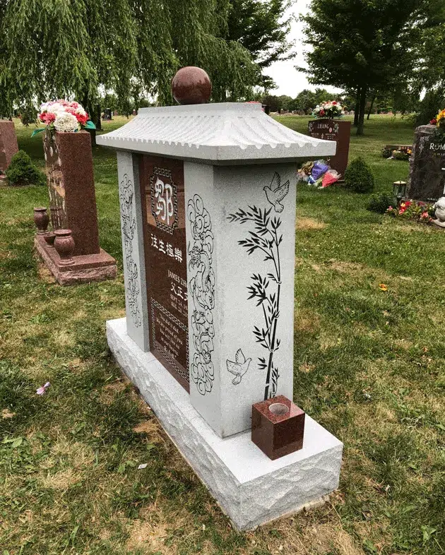 Gray granite family columbarium from an angle, with a tiled Asian roof, red sphere and etched bamboo and doves on the side