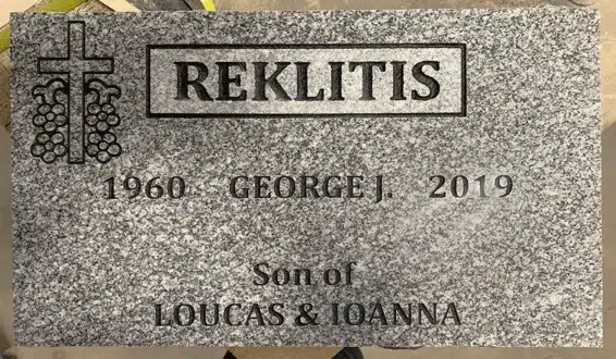 Gray granite flat marker with a cross wrapped in grapevines, a boxed family name, a given name and years