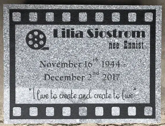 Gray granite flat marker with a filmstrip border and film reel emblem, engraved name, dates and a short quote