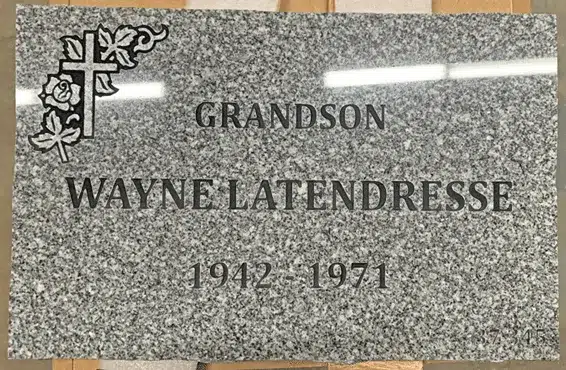 Grey granite flat grave marker with a carved cross and rose at the top left, a family relationship, a name and years