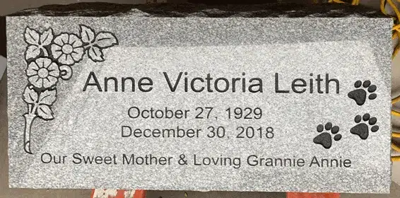 Light grey granite flat marker with a carved morning glory spray, three paw prints, a name, dates and a tribute line