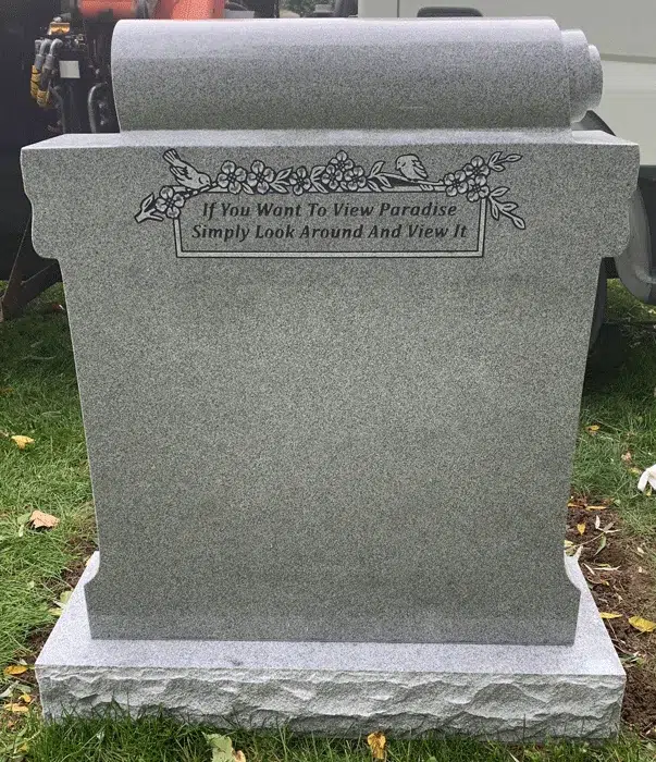 Grey granite upright headstone with a carved scroll top, engraved songbirds on blossom branches and a two line epitaph