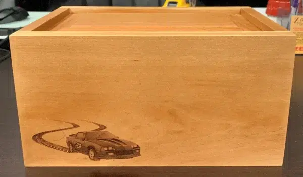 Laser Engraved Wood Urn with Sports Car Laser engraved honey toned wood urn with a sports car and winding tire tracks at the lower left corner