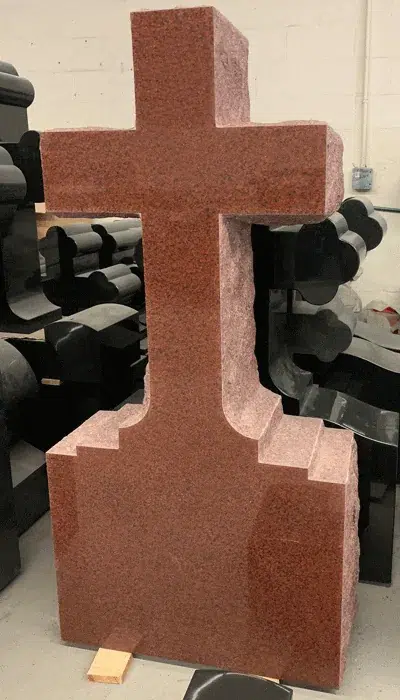 Red granite Latin cross monument with a blank polished face and stepped shoulders on a rough edged base block