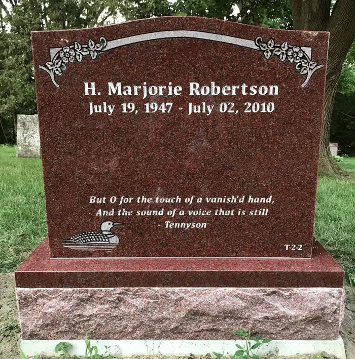 Red granite upright headstone with a floral scroll border and an engraved loon