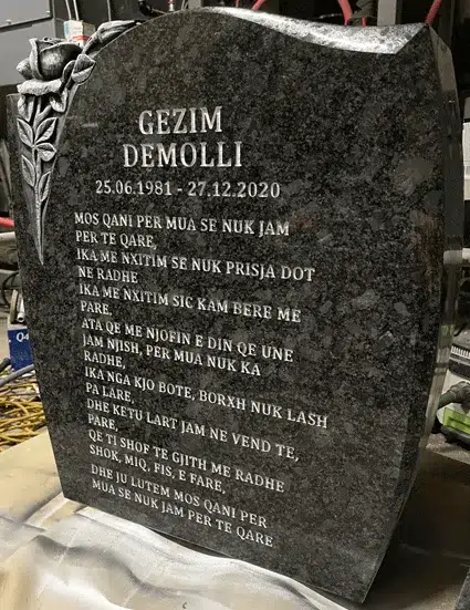 Silver Bronze granite headstone seen at an angle, with a carved rose at the corner and an engraved name, dates and epitaph