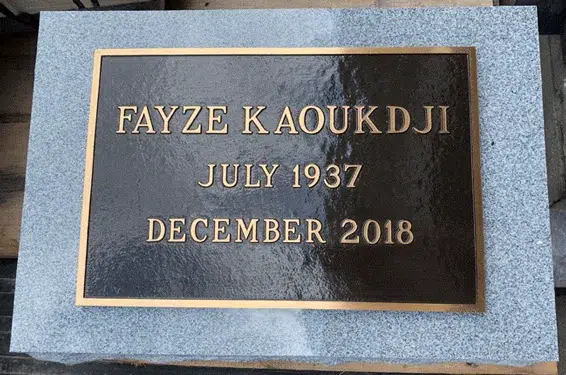 Simple bronze grave marker on a light grey granite base, plain border and raised lettering with a name and dates